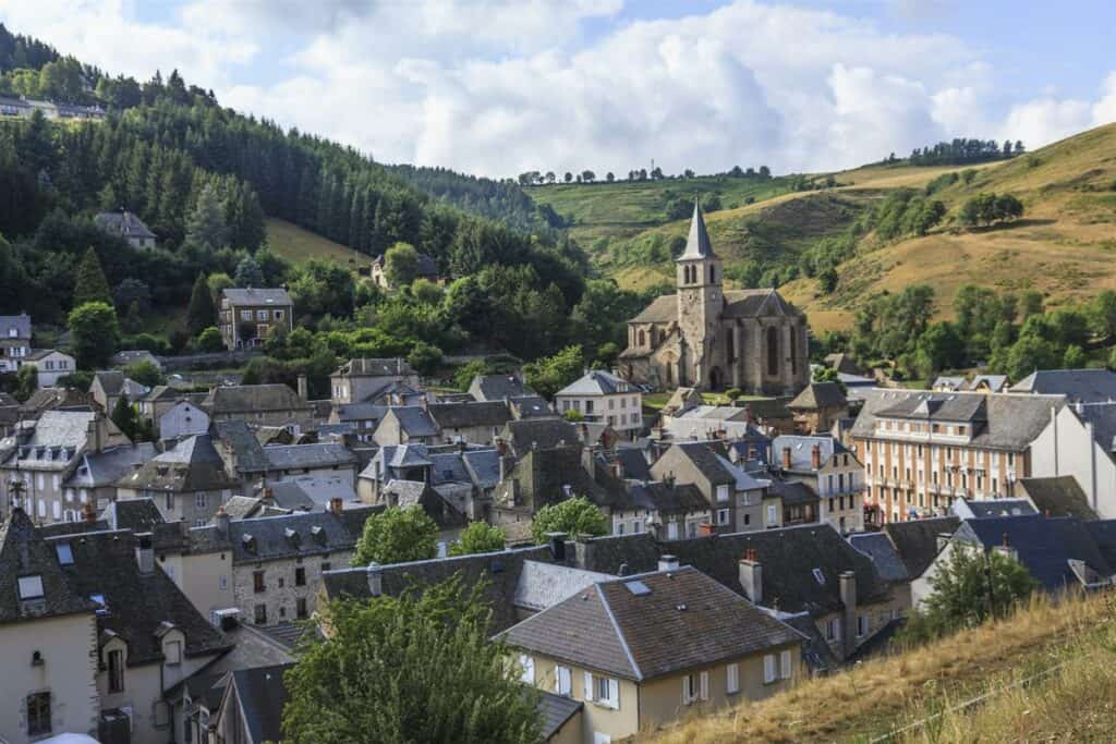 Paysage de Chaudes-Aigues avec maisons traditionnelles et collines verdoyantes.
