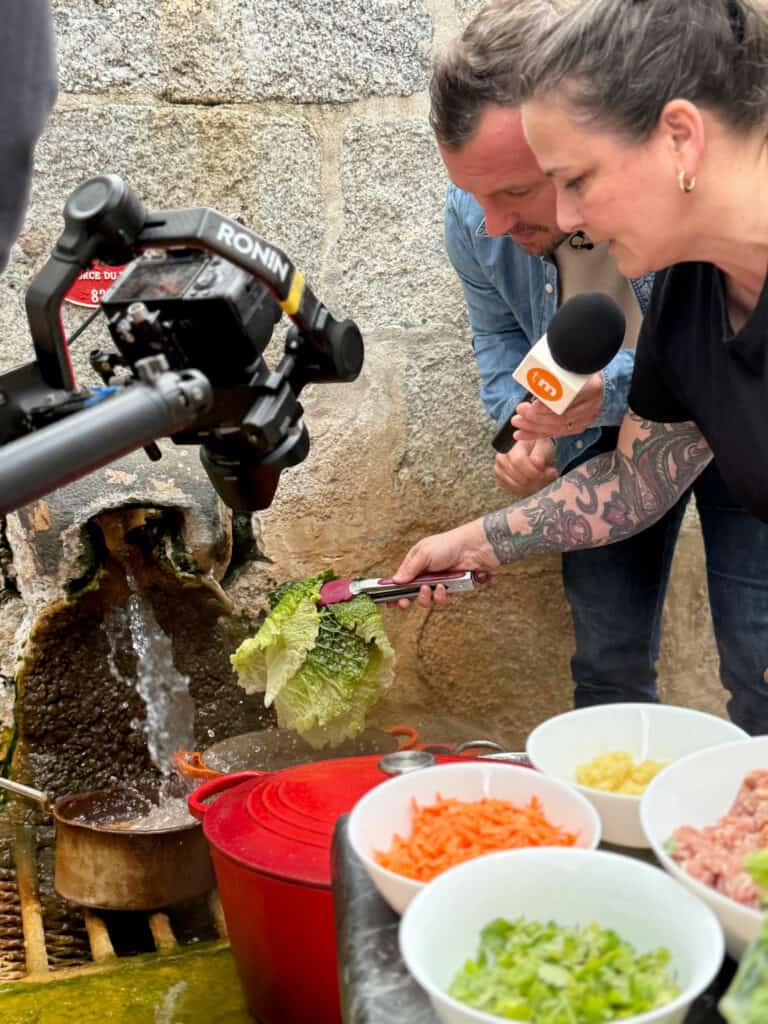 Cécile Chaudesaigues et Loïc Ballet blanchissent des feuilles de chou dans l'eau chaude de la Source du Par à Chaudes-Aigues lors d'un tournage pour Télématin.
