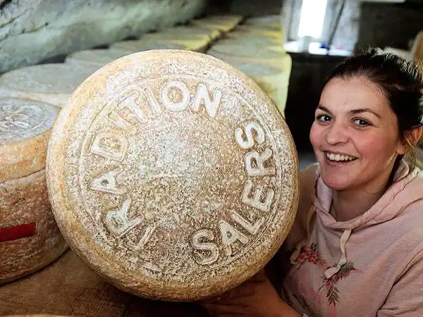 Charlotte Salat aux côtés d’une tomme portant la marque Salers dans sa cave d’affinage.